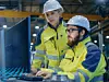 Zwei Mitarbeiter stehen in einer Industriehalle vor einem Computer und arbeiten daran