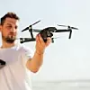 Young man holding drone before flight near ocean or sea. Pretty guy prepare to pilot outdoor