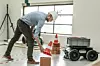 Ein Forscher platziert im Labor Hindernisse wie Ziegelsteine für einen vierrädrigen Bauroboter. Der Roboter soll lernen, sich auf Baustellen zu orientieren.