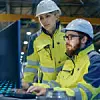 Zwei Mitarbeiter stehen in einer Industriehalle vor einem Computer und arbeiten daran