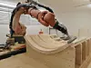 Ein Kuka Roboter bearbeitet in einer Tischlerei ein großes Holzstück.
