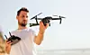 Young man holding drone before flight near ocean or sea. Pretty guy prepare to pilot outdoor