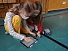 Schülerinnen programmieren Roboter am Tablet auf Turnhallen-Boden