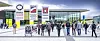 Besucher laufen vor einer modernen Messehalle mit Glasfront und mehreren Werbebannern. Gemeint ist die Messe Stuttgart als Veranstaltungsort der MOTEK. Anlaufbild für das Themenspecial zu dieser Messe.